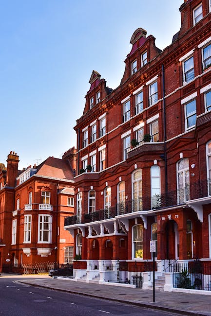 A row of brightly coloured terraced houses along a quiet street in North Kensington, London, featuring pastel blue, yellow, and lavender facades with white window frames and black wrought iron railing